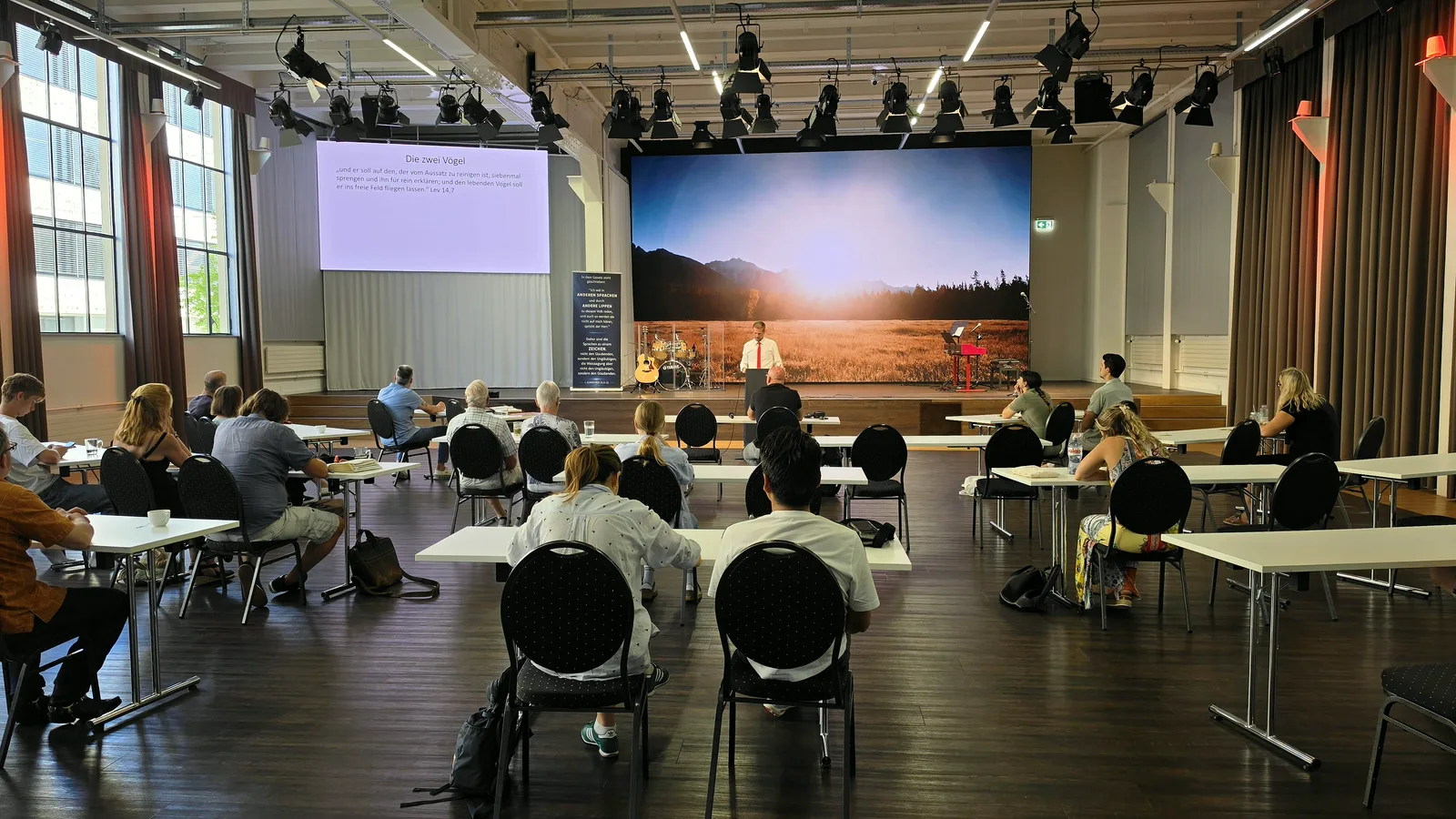 Sonntagsgottesdienst im Christlichen Zentrum Bern: die Gemeinde sitzt an Tischen, vorne die Predigt vor der grossen LED-Wand